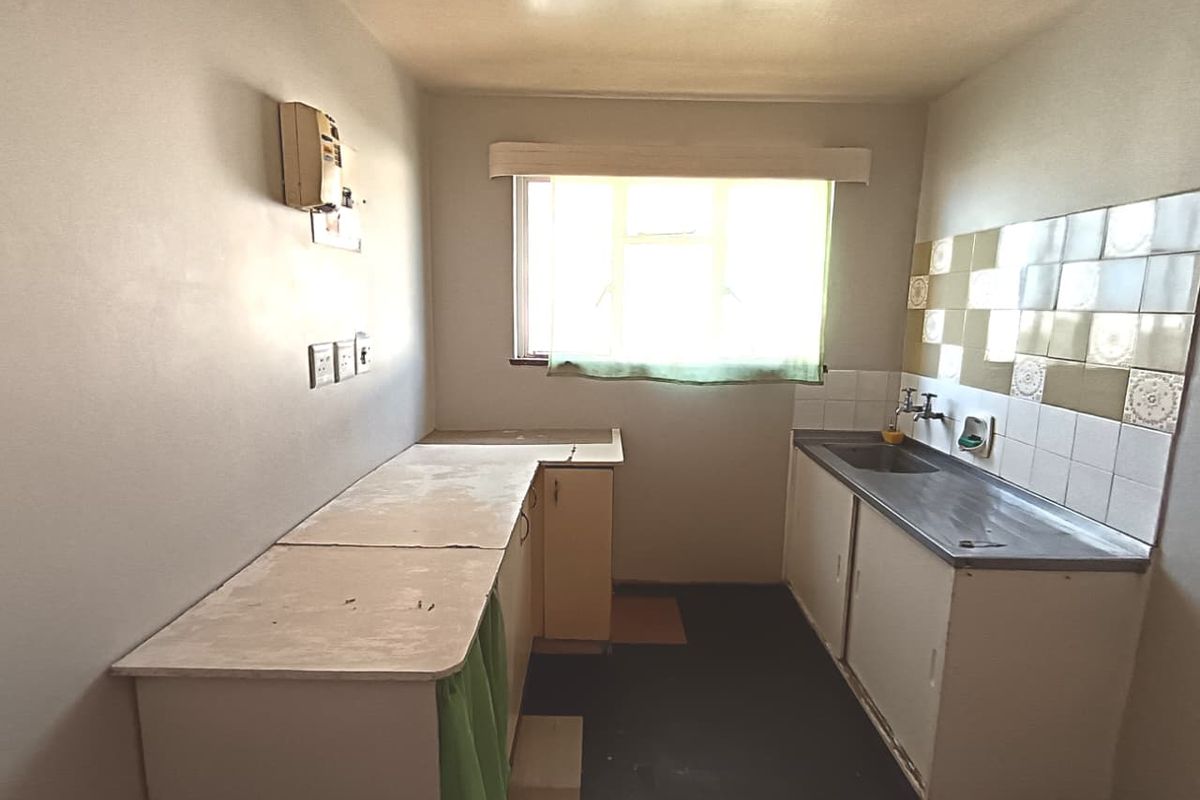 A functional, dated kitchen featuring built-in cabinetry, a stainless steel sink, and tiled splashbacks, offering a blank canvas for modern renovation.