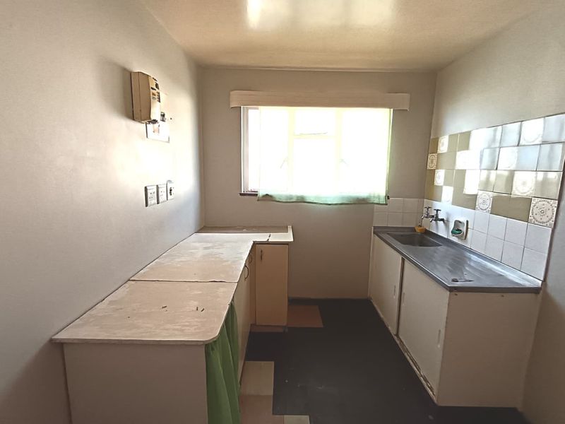 A functional, dated kitchen featuring built-in cabinetry, a stainless steel sink, and tiled splashbacks, offering a blank canvas for modern renovation.