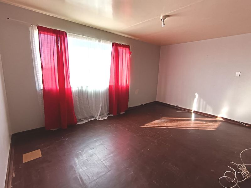 An empty living room featuring dark timber flooring and a large window, presenting a blank canvas for renovation and interior design updates.