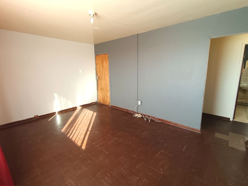 An empty living room featuring dark parquet flooring, a wooden door, and visible surface-mounted electrical conduit on the grey feature wall.