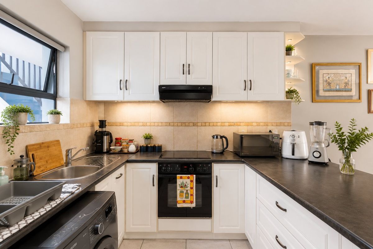 A well-maintained kitchen featuring white cabinetry, dark countertops, integrated appliances, and a tiled backsplash with convenient under-cabinet lighting.