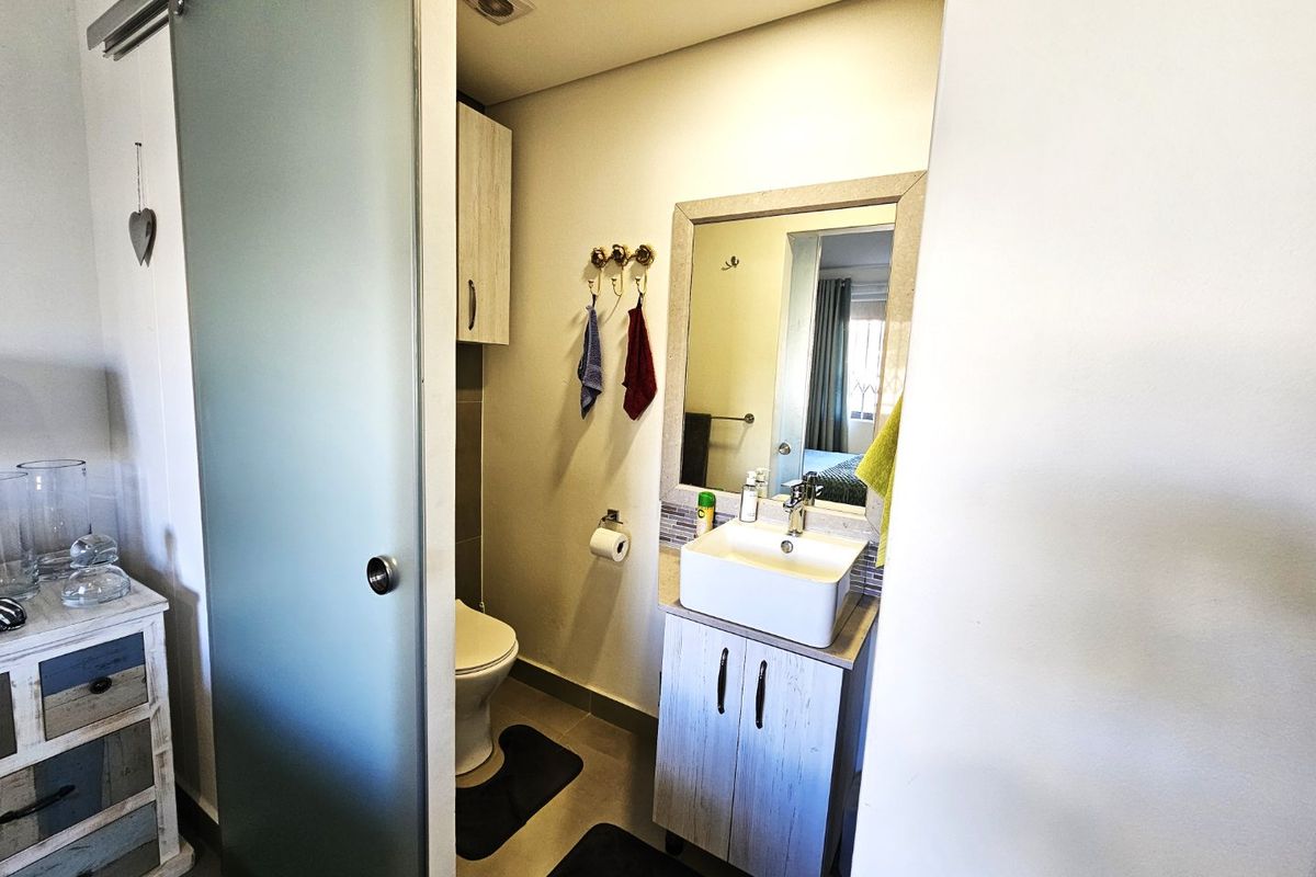 A compact bathroom featuring a modern vessel sink on a vanity cabinet, a frosted glass sliding door, and a wall-mounted mirror.