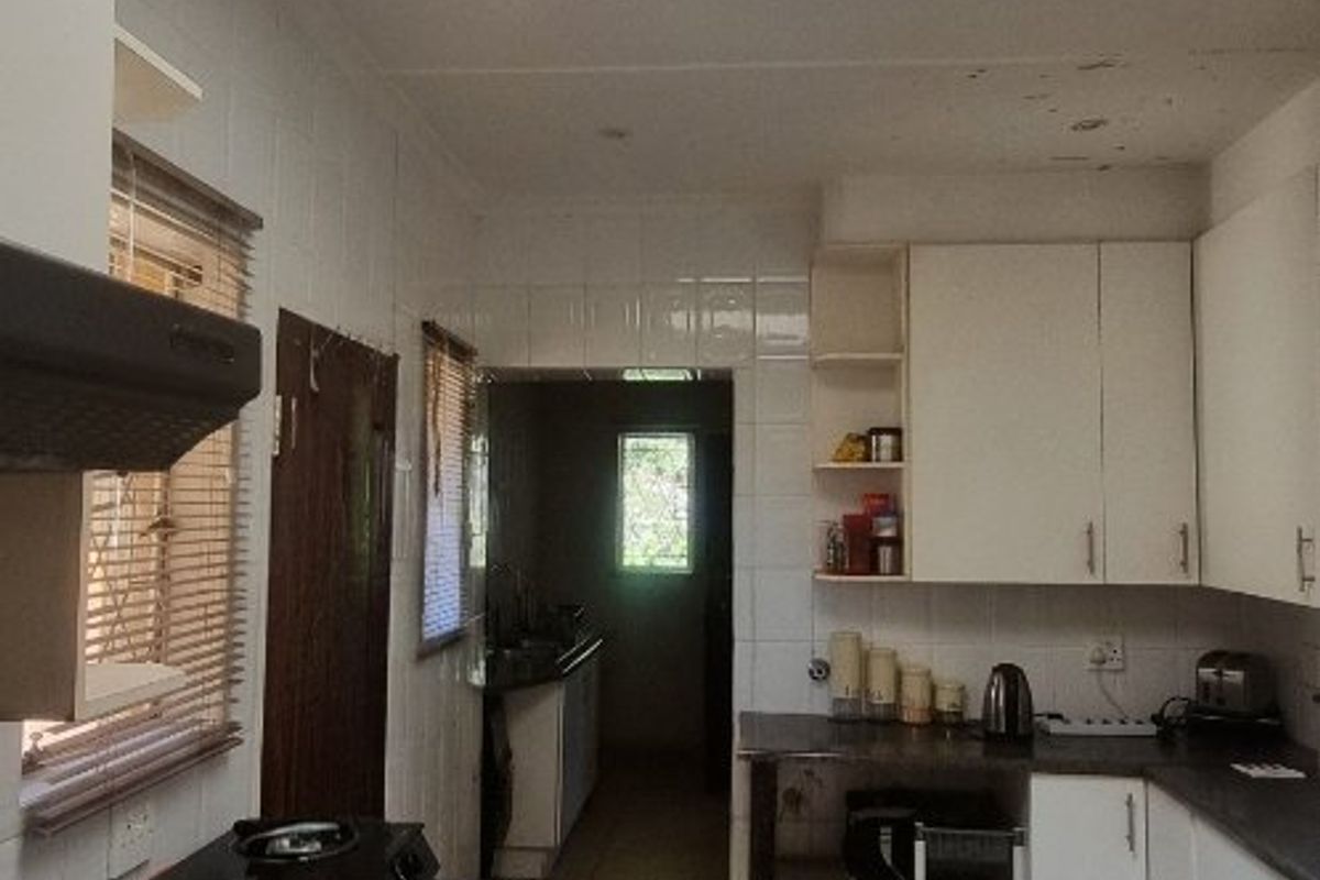 A functional kitchen featuring tiled flooring, built-in cabinetry, laminate countertops, and a skylight providing natural light. Shows signs of wear on the ceiling.