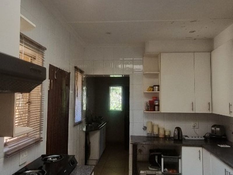 A functional kitchen featuring tiled flooring, built-in cabinetry, laminate countertops, and a skylight providing natural light. Shows signs of wear on the ceiling.
