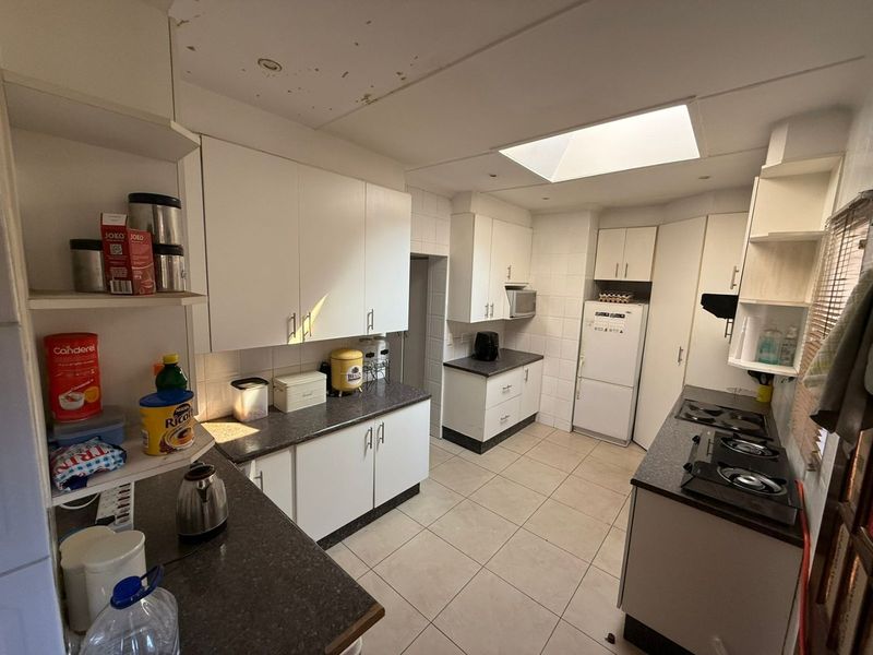 A functional kitchen featuring white cabinetry, dark laminate countertops, a built-in hob, and a skylight, requiring some ceiling maintenance.