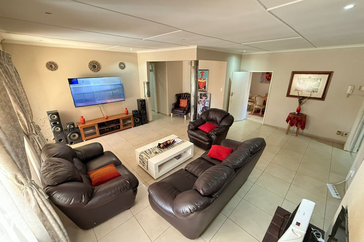 Spacious living room featuring neutral tiled flooring, recessed ceiling lighting, and an open-plan layout connecting to adjacent living areas.