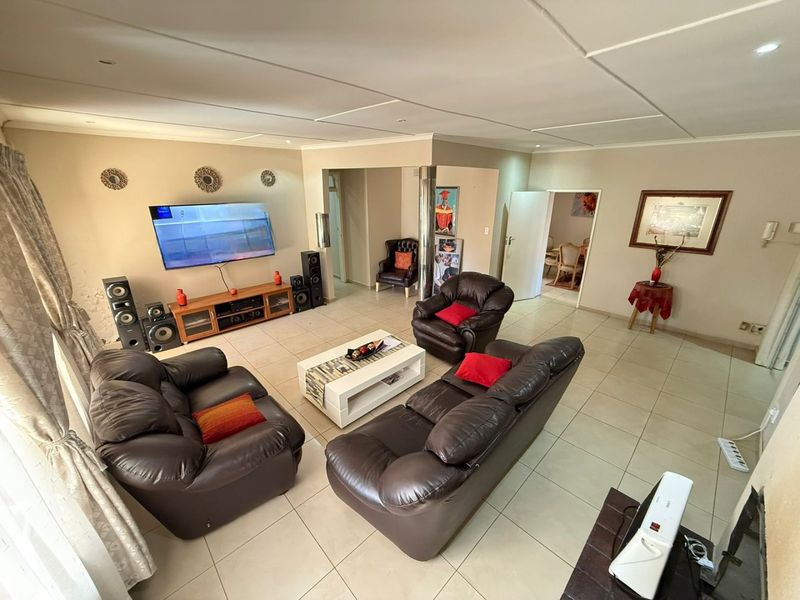 Spacious living room featuring neutral tiled flooring, recessed ceiling lighting, and an open-plan layout connecting to adjacent living areas.