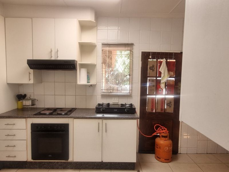 A functional kitchen featuring white cabinetry, a combination of electric and gas hobs, an integrated oven, and tiled finishes throughout.
