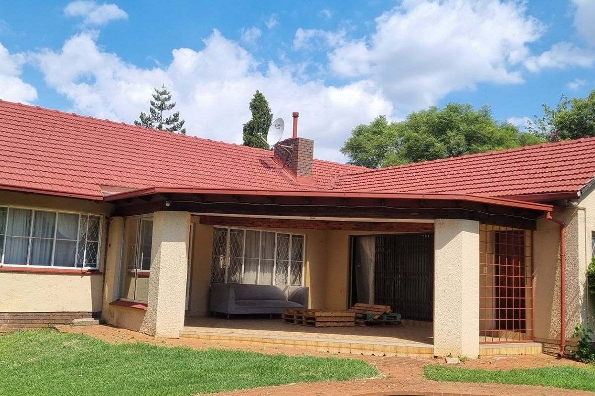 Rear view of a single-story house featuring a covered patio, tiled roof, and a spacious garden area.
