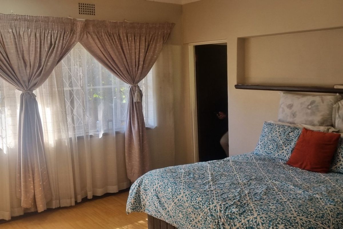 A bedroom featuring laminate flooring, a built-in wall niche for storage, and windows fitted with security burglar bars.