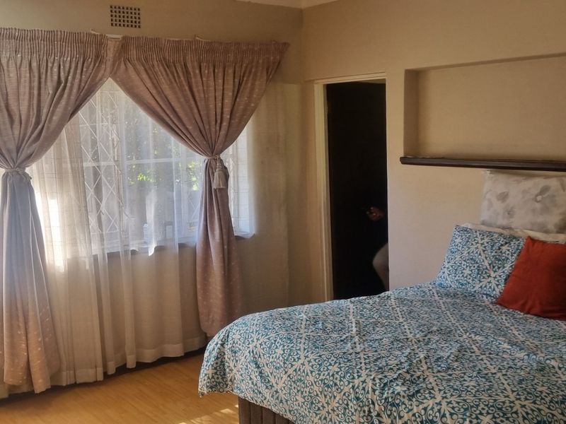 A bedroom featuring laminate flooring, a built-in wall niche for storage, and windows fitted with security burglar bars.