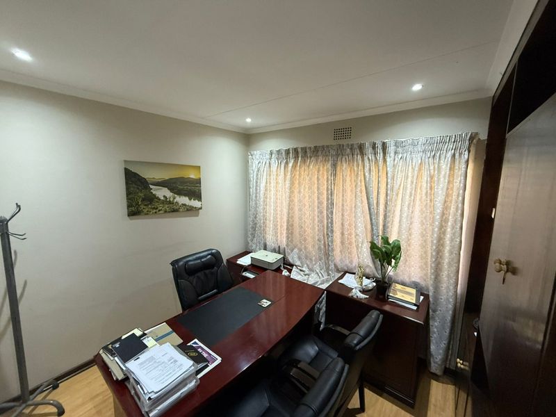 A functional home office space featuring laminate flooring, recessed downlighting, and a built-in storage cupboard.