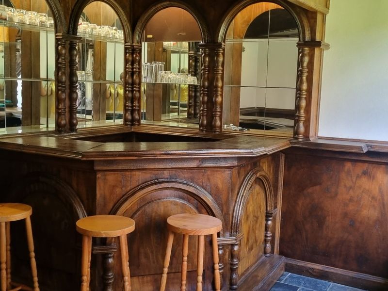 A dedicated home bar area featuring custom built-in wooden cabinetry, a mirrored back bar, and durable stone tile flooring.