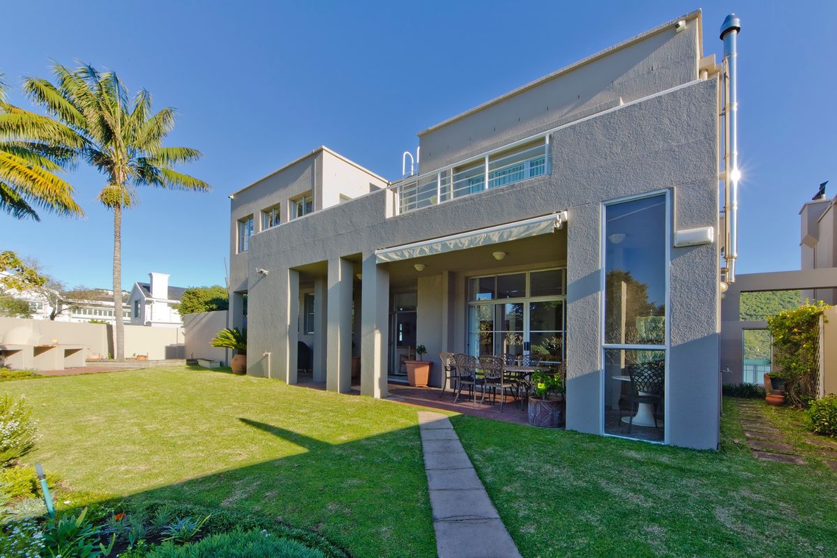 Rear view of a modern multi-story house featuring a covered patio, upper-level balcony, and a well-maintained garden with a paved walkway.