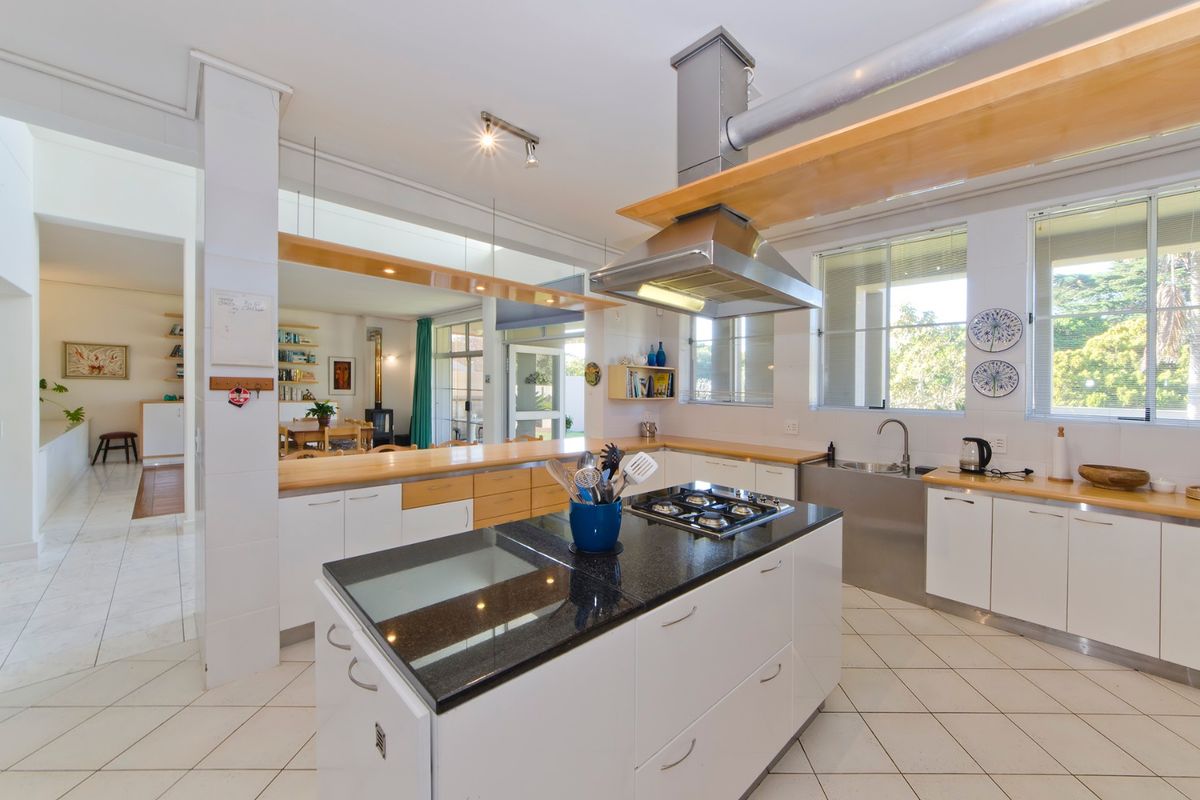 Spacious kitchen featuring a central island with gas cooktop, stainless steel extractor fan, wooden countertops, and ample built-in cabinetry, flowing into the living area.