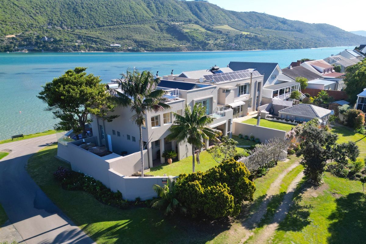 Aerial view of a waterfront property featuring solar panels, solar water heating, landscaped gardens, and a balcony overlooking the lagoon.