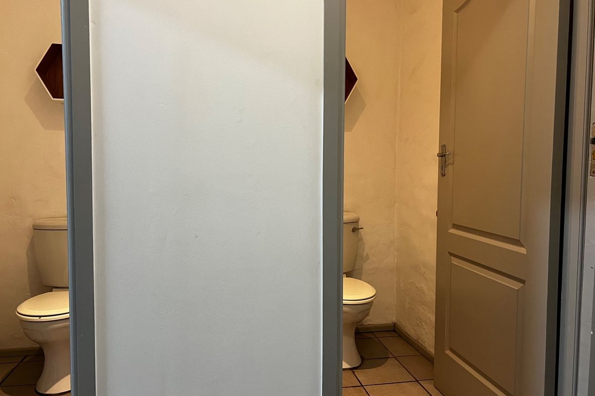 A functional bathroom space featuring two toilets separated by a partition wall, with tiled flooring and visible wall surface wear.