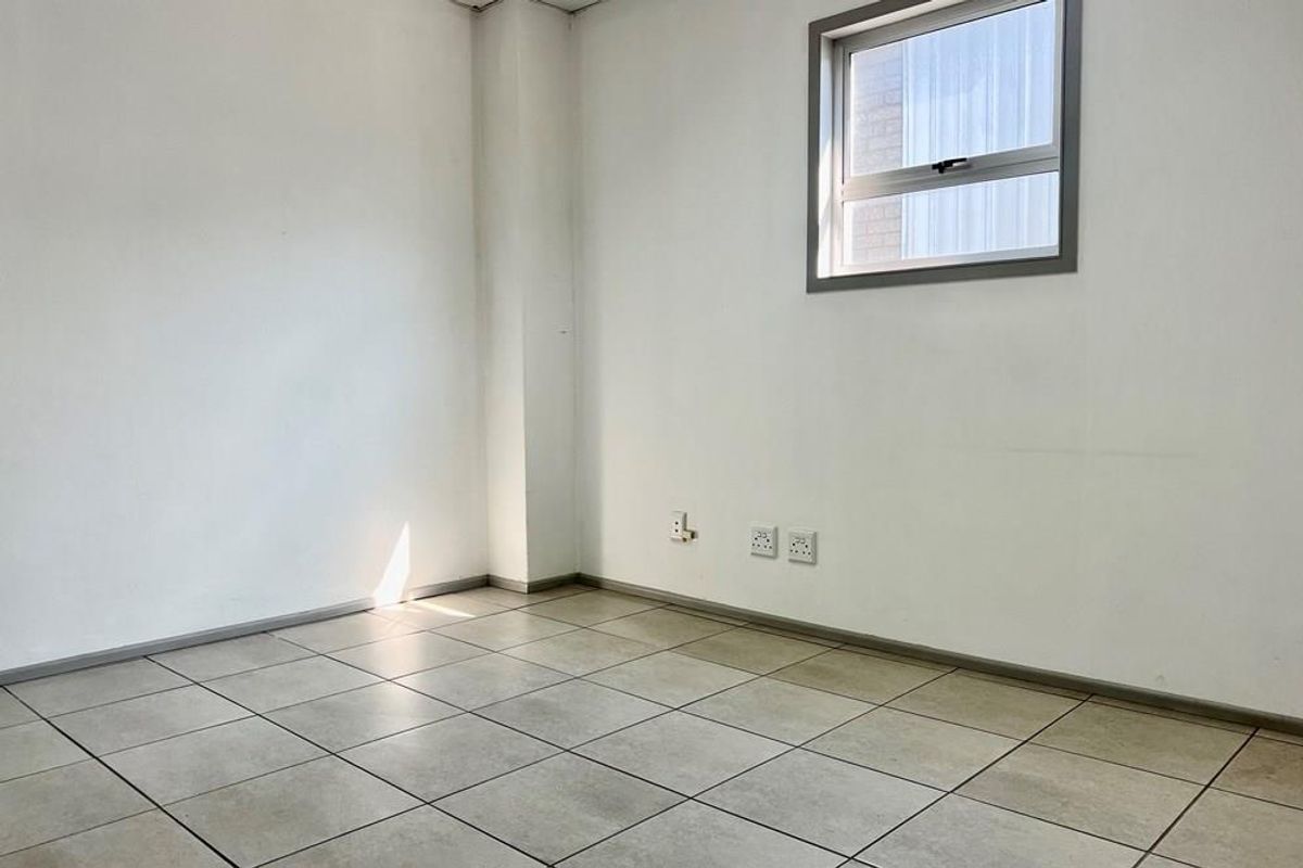 A vacant commercial office space featuring neutral tiled flooring, white walls, and a single window, providing a clean and functional workspace.