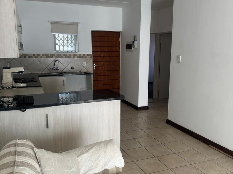 Open plan living area featuring a functional kitchen with granite countertops, tiled backsplash, and neutral ceramic floor tiles throughout the space.