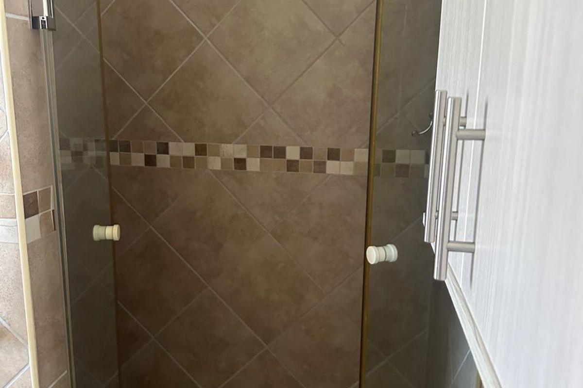A compact shower stall featuring neutral-toned wall tiles with a mosaic accent border and a matching mosaic tiled floor.