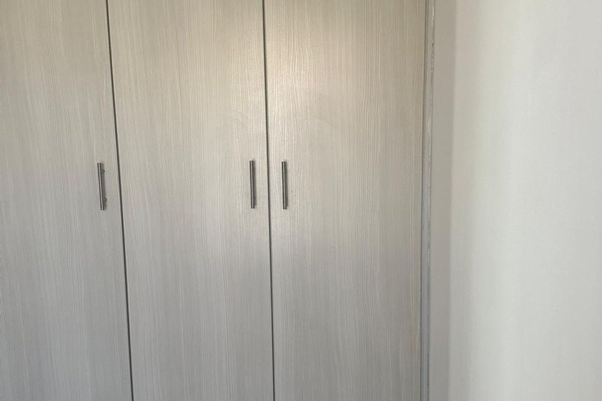 A bedroom featuring a modern, light-toned built-in wardrobe with sleek metal handles and neutral carpeting.