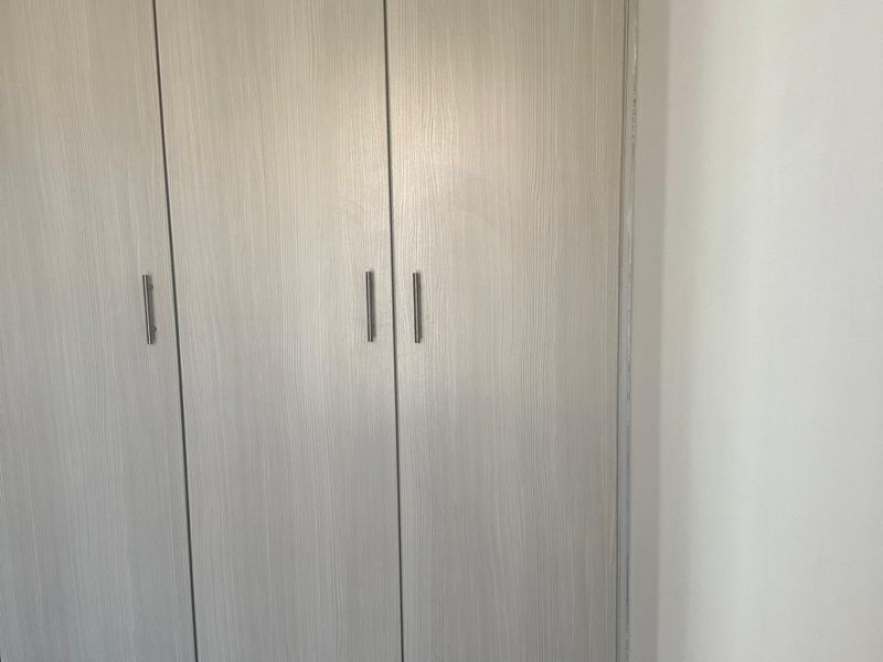 A bedroom featuring a modern, light-toned built-in wardrobe with sleek metal handles and neutral carpeting.