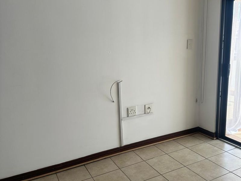 An empty living area featuring tiled flooring, a sliding glass door, and visible surface-mounted electrical wiring and outlets.