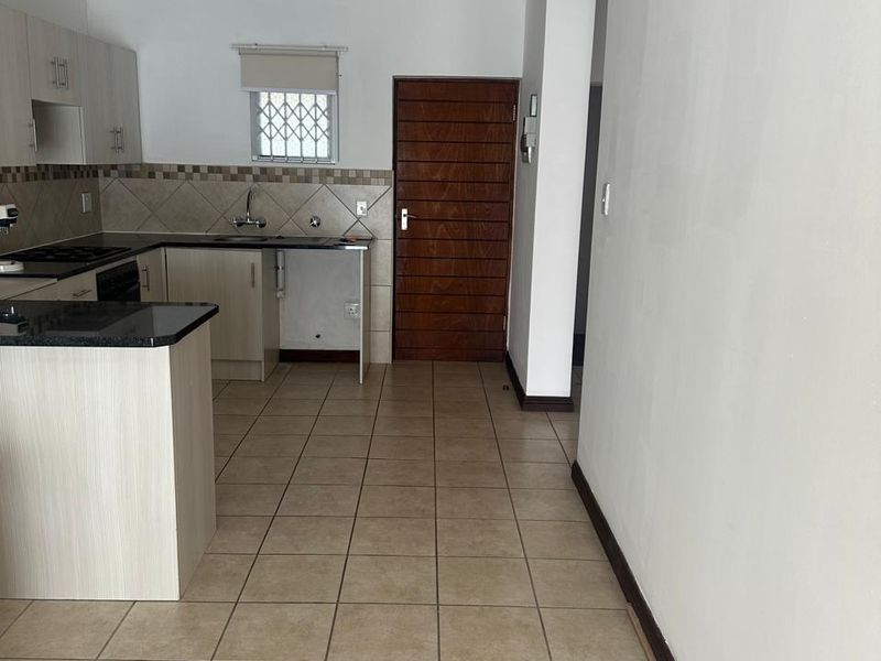 A functional kitchen featuring built-in cabinetry, granite countertops, a tiled backsplash, and ceramic floor tiling, presented in a clean, empty state.