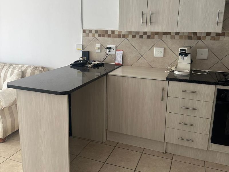 A functional kitchen area featuring light wood-grain cabinetry, dark granite countertops, a tiled backsplash, and ceramic floor tiles.