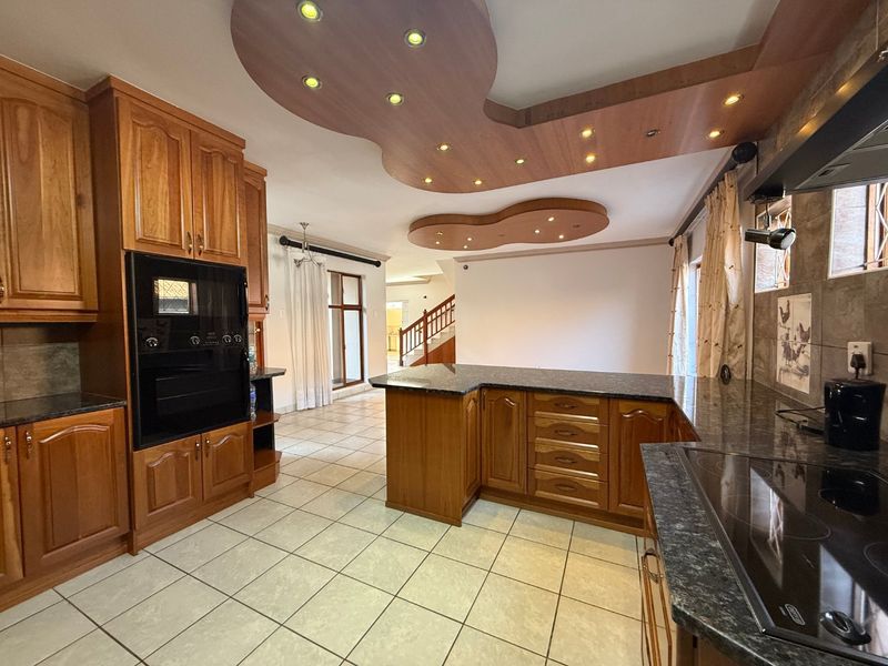 Spacious kitchen featuring extensive wooden cabinetry, granite countertops, built-in oven, electric hob, and a unique decorative recessed ceiling with integrated lighting.