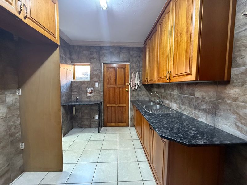 A functional kitchen featuring wooden cabinetry, granite countertops, a double stainless steel sink, and full-height wall tiling.