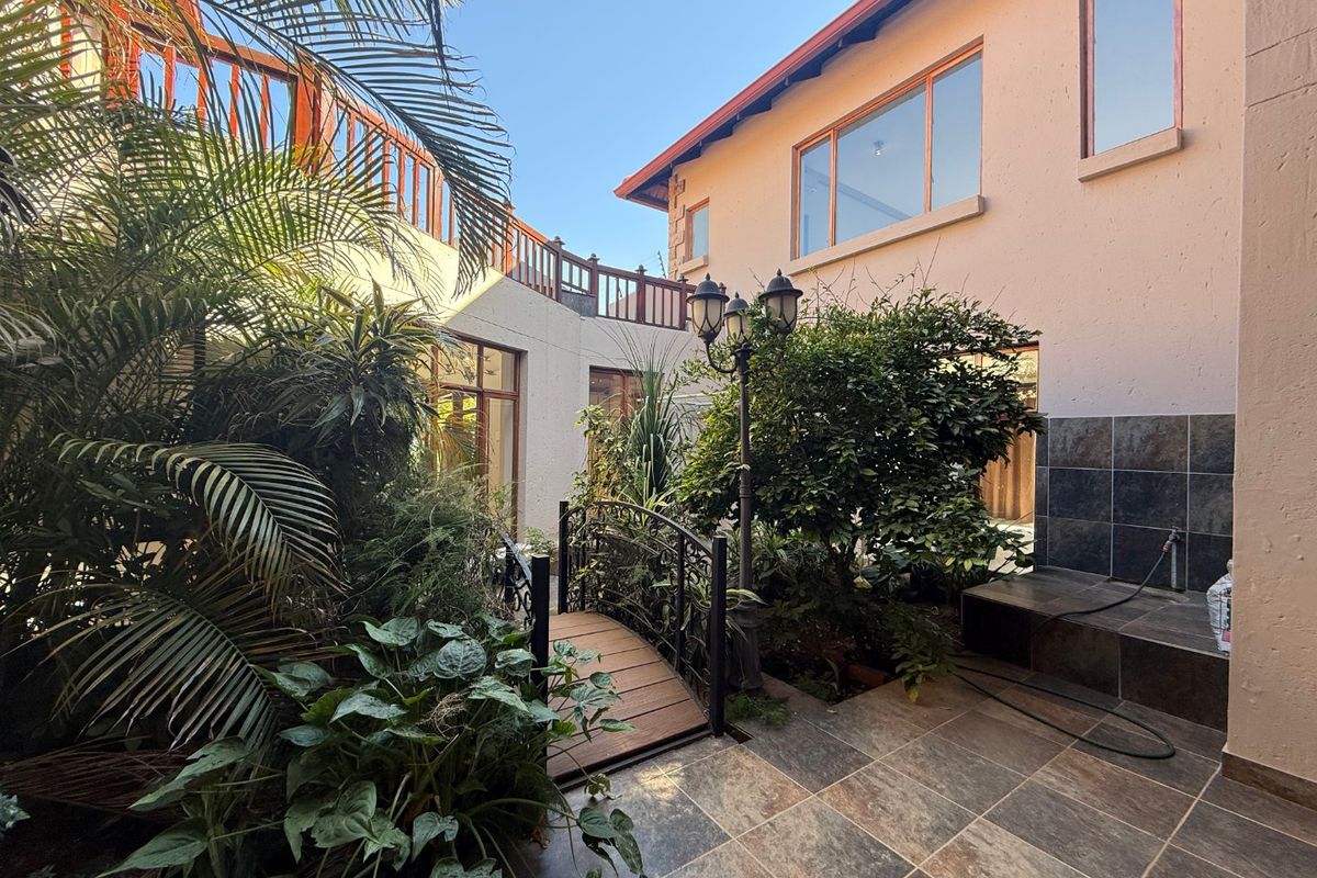 A landscaped rear courtyard featuring a tiled patio, a decorative wooden bridge, and a raised wooden balcony overlooking the garden area.