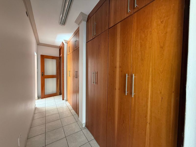 A clean, well-maintained hallway featuring extensive built-in wooden cabinetry for storage and neutral tiled flooring.