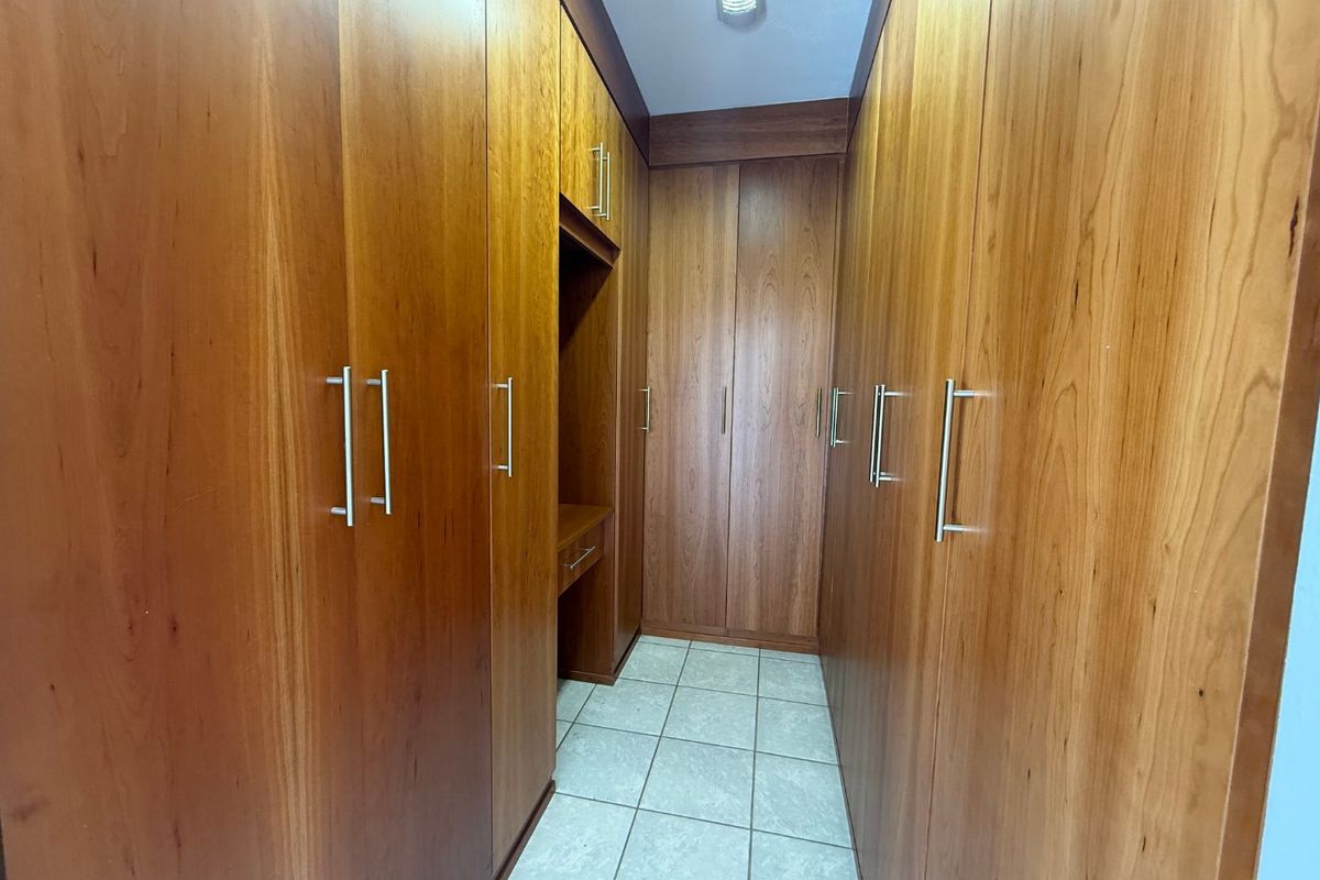 A walk-in closet or dressing area featuring extensive floor-to-ceiling wooden built-in cabinetry, integrated vanity desk, and neutral tiled flooring.