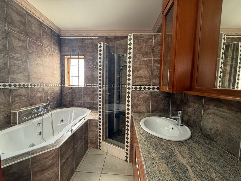 A spacious bathroom featuring a built-in bathtub, separate shower enclosure, and a vanity with granite countertop and wooden cabinetry.