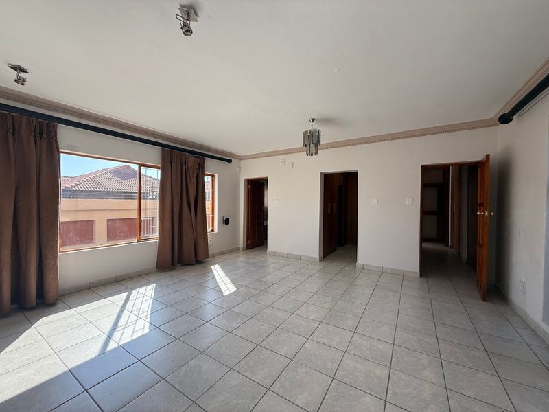 A spacious, sunlit living area featuring neutral tiled flooring, classic cornice detailing, and multiple doorways leading to other parts of the home.
