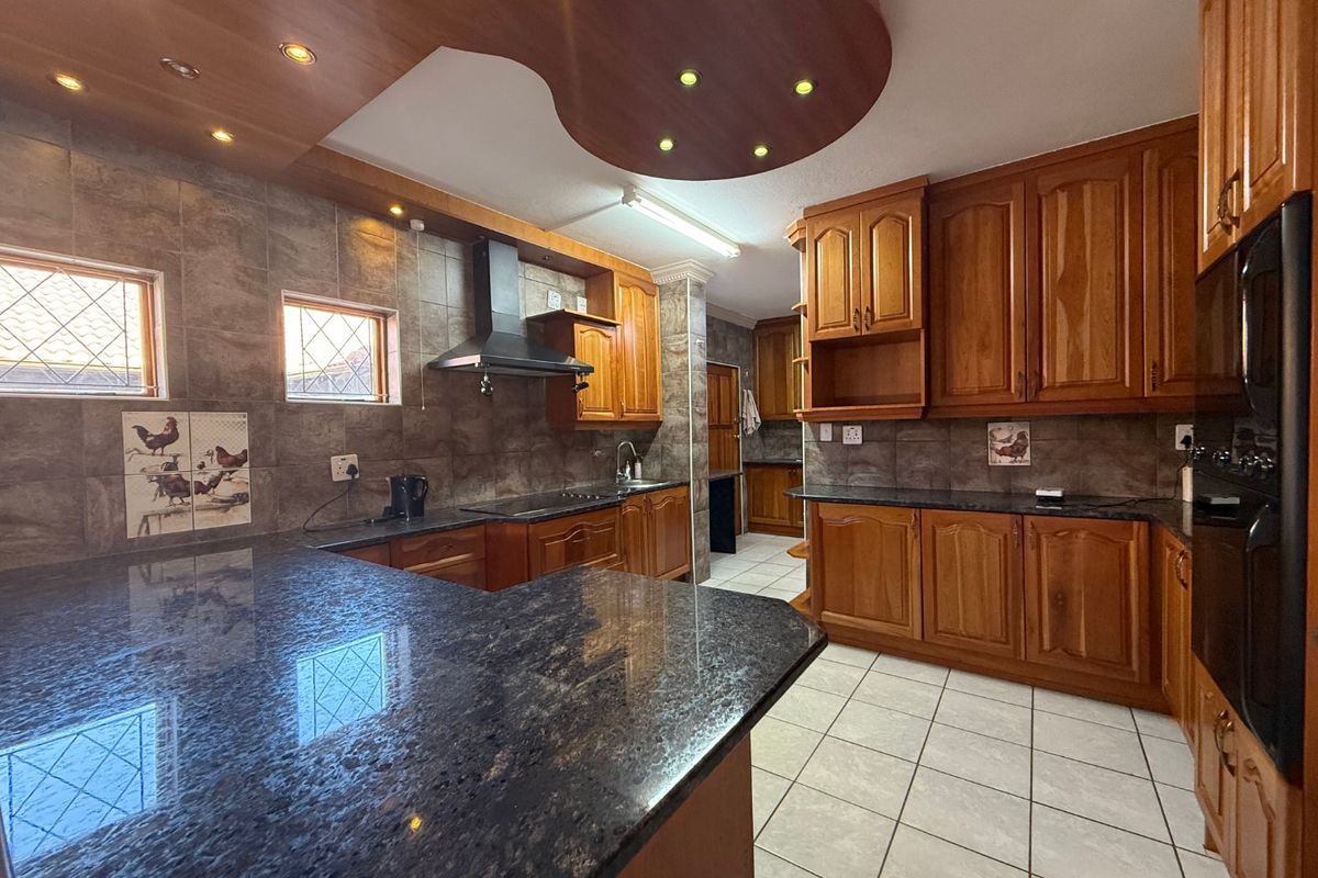 Spacious kitchen featuring extensive wooden cabinetry, dark granite countertops, a tiled backsplash, and integrated lighting within a decorative ceiling feature.