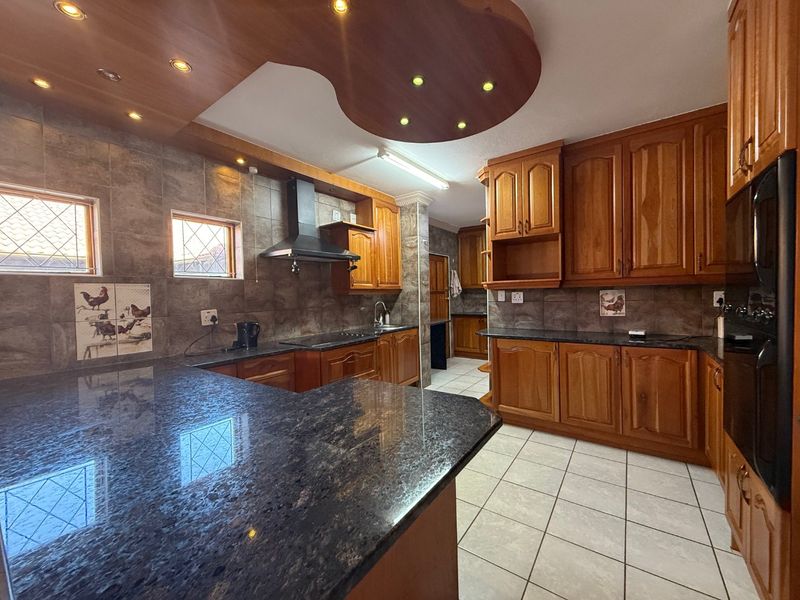 Spacious kitchen featuring extensive wooden cabinetry, dark granite countertops, a tiled backsplash, and integrated lighting within a decorative ceiling feature.