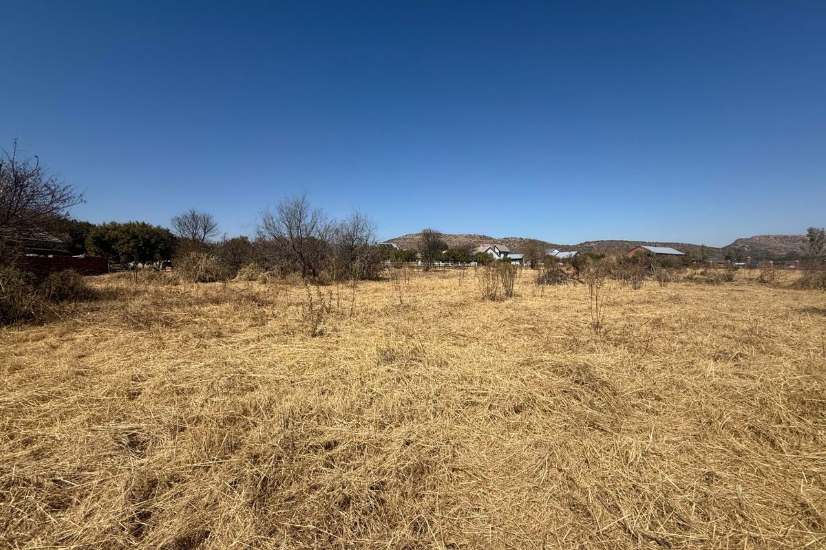 A wide-angle view of a vacant residential plot featuring dry natural vegetation and open space with distant rural surroundings.