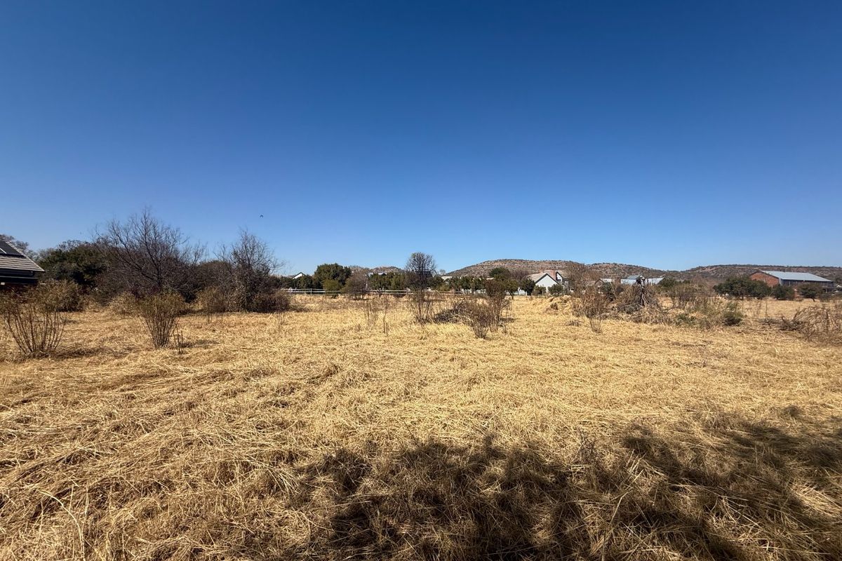 A wide-angle view of a vacant residential plot featuring dry natural grass and surrounding landscape.