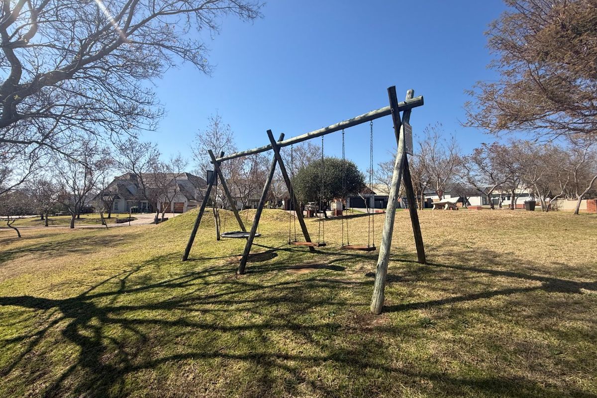 A spacious residential garden area featuring a wooden swing set and established trees on a well-maintained lawn.