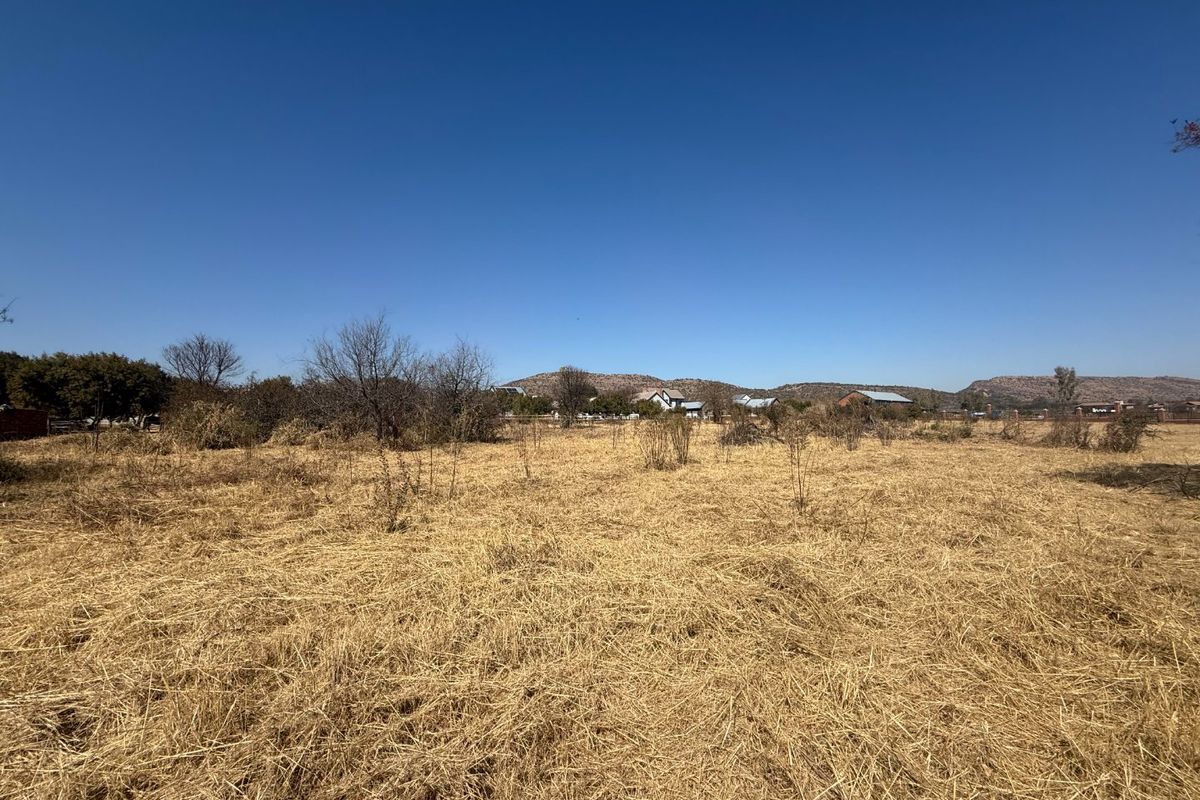 A wide-angle view of a vacant residential plot featuring dry grass and natural vegetation with distant mountain views.