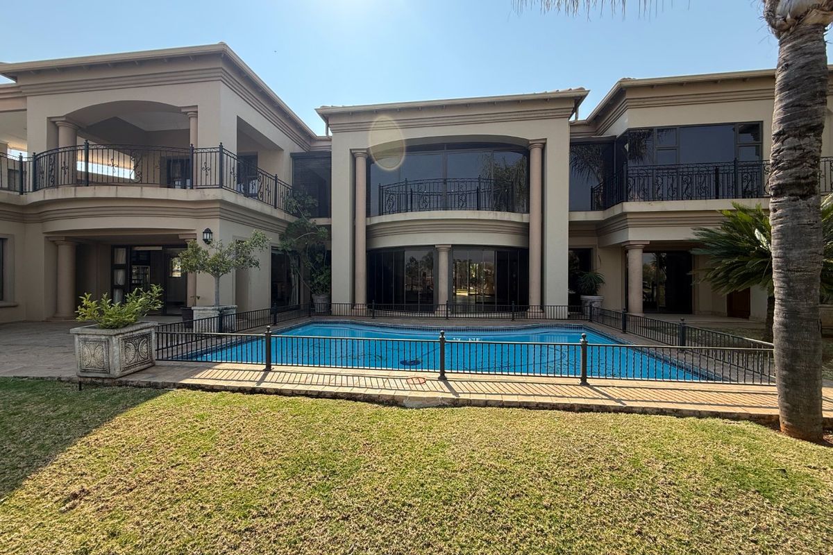 A spacious rear exterior view featuring a large swimming pool, manicured lawn, and a multi-level residence with covered balconies and classic architectural columns.