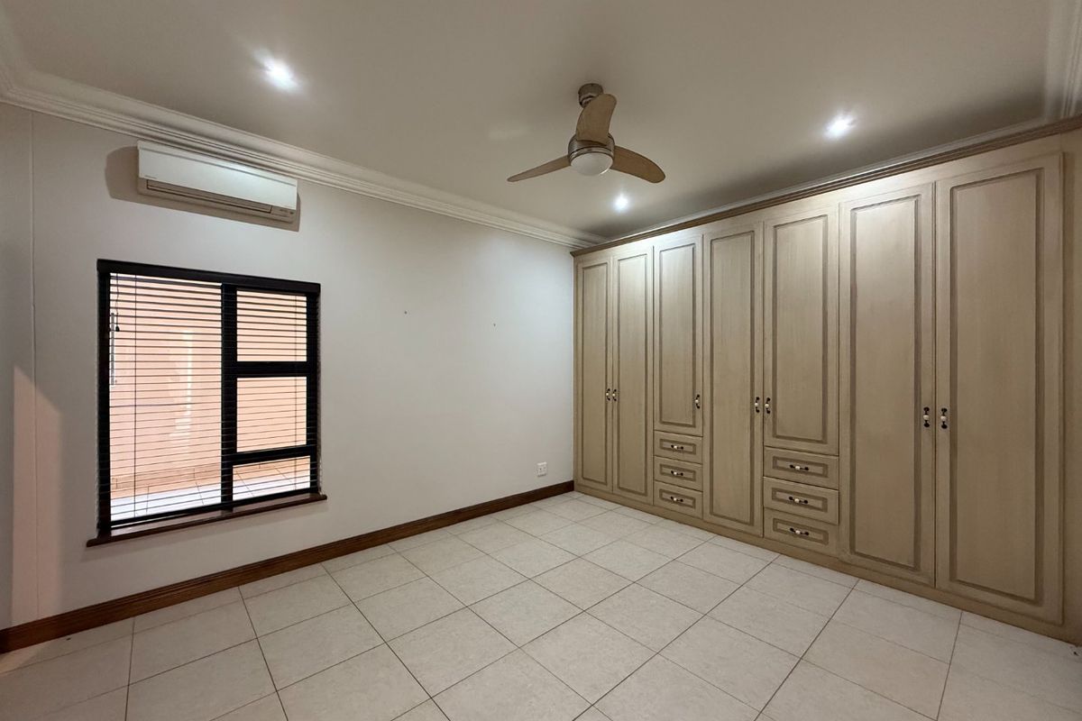 A well-maintained bedroom featuring extensive built-in cabinetry, tiled flooring, a ceiling fan, and a wall-mounted air conditioning unit.