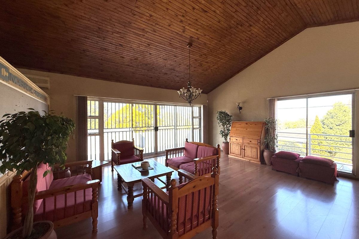 Spacious living room featuring a high vaulted timber ceiling, laminate flooring, and large sliding glass doors with security bars providing ample natural light.