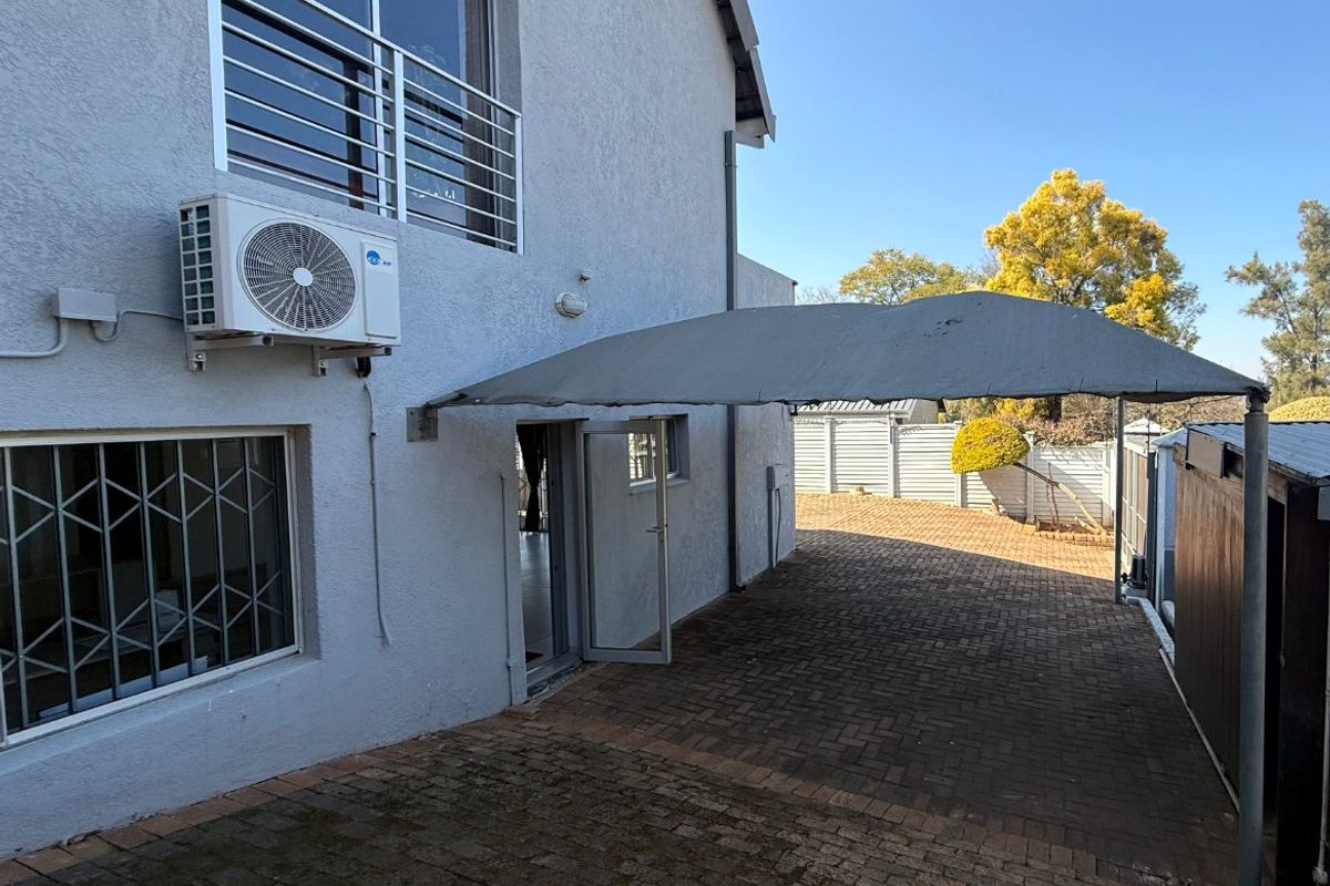 Rear exterior view of the property featuring a paved area, shade sail, and wall-mounted air conditioning unit.