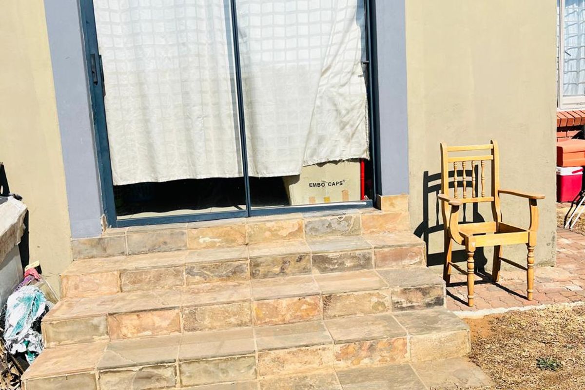 Rear exterior view of the townhouse featuring a sliding glass door with tiled steps leading to the garden area.