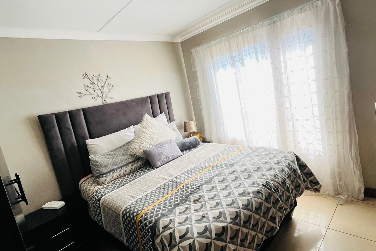 A well-maintained bedroom featuring tiled flooring, decorative cove cornicing, and a large sliding glass door providing natural light.