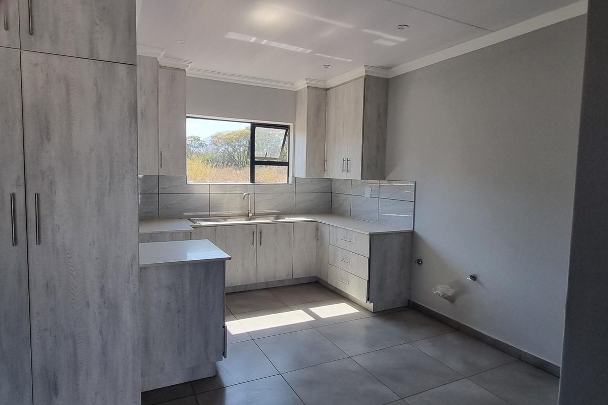 A modern, empty kitchen featuring light wood-grain cabinetry, tiled backsplash, tiled flooring, and plumbing connections ready for appliance installation.