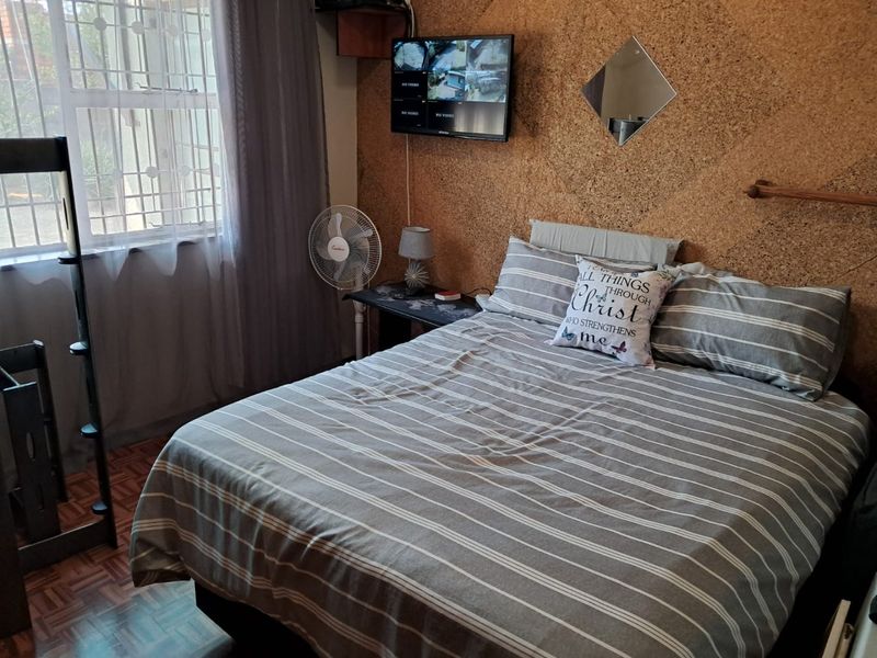 A bedroom featuring parquet flooring and distinctive cork wall cladding, equipped with security bars on the window.